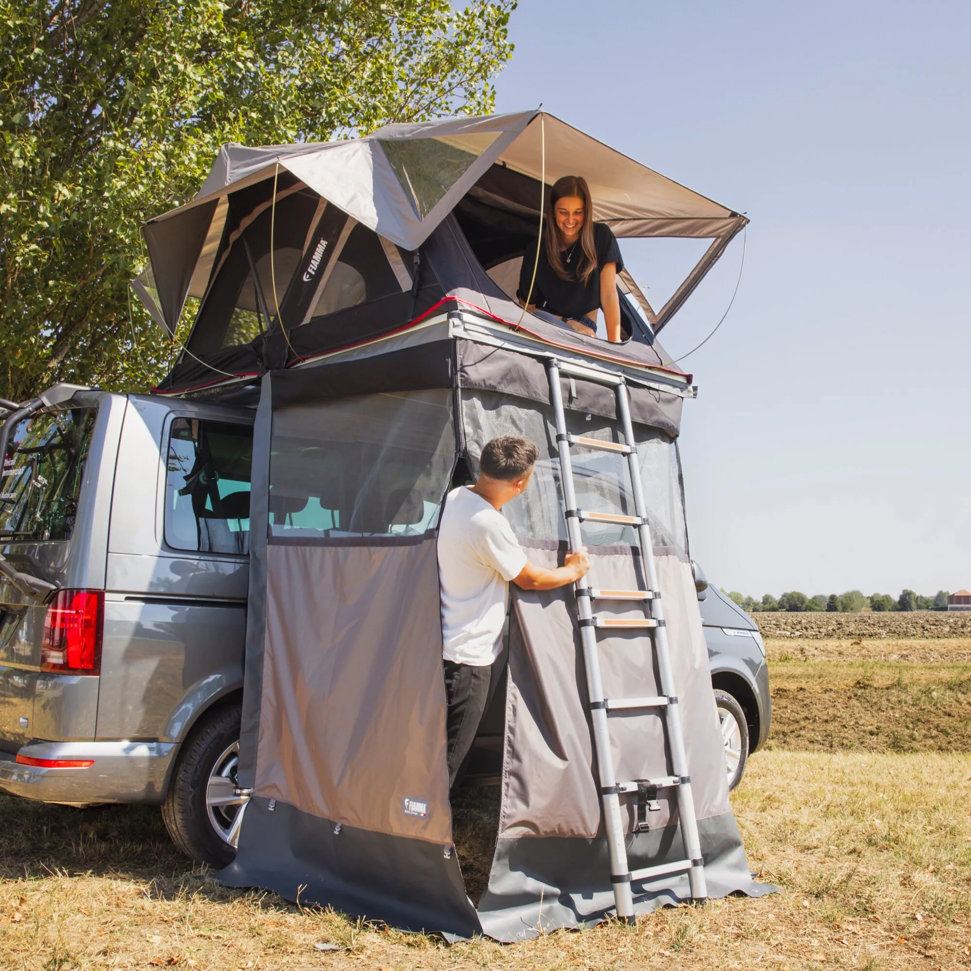 Graues Privacy Moonlight Tent von Fiamma als Umkleideraum am Fahrzeug mit Leiter und zwei Personen geschniegelt