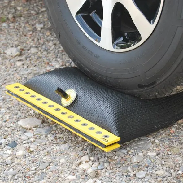 Schwarzes Ausgleichskissen EMUK Air-Lift® unter einem Fahrzeugreifen auf Schotter, mit gelber Auffahrschiene und Ventil