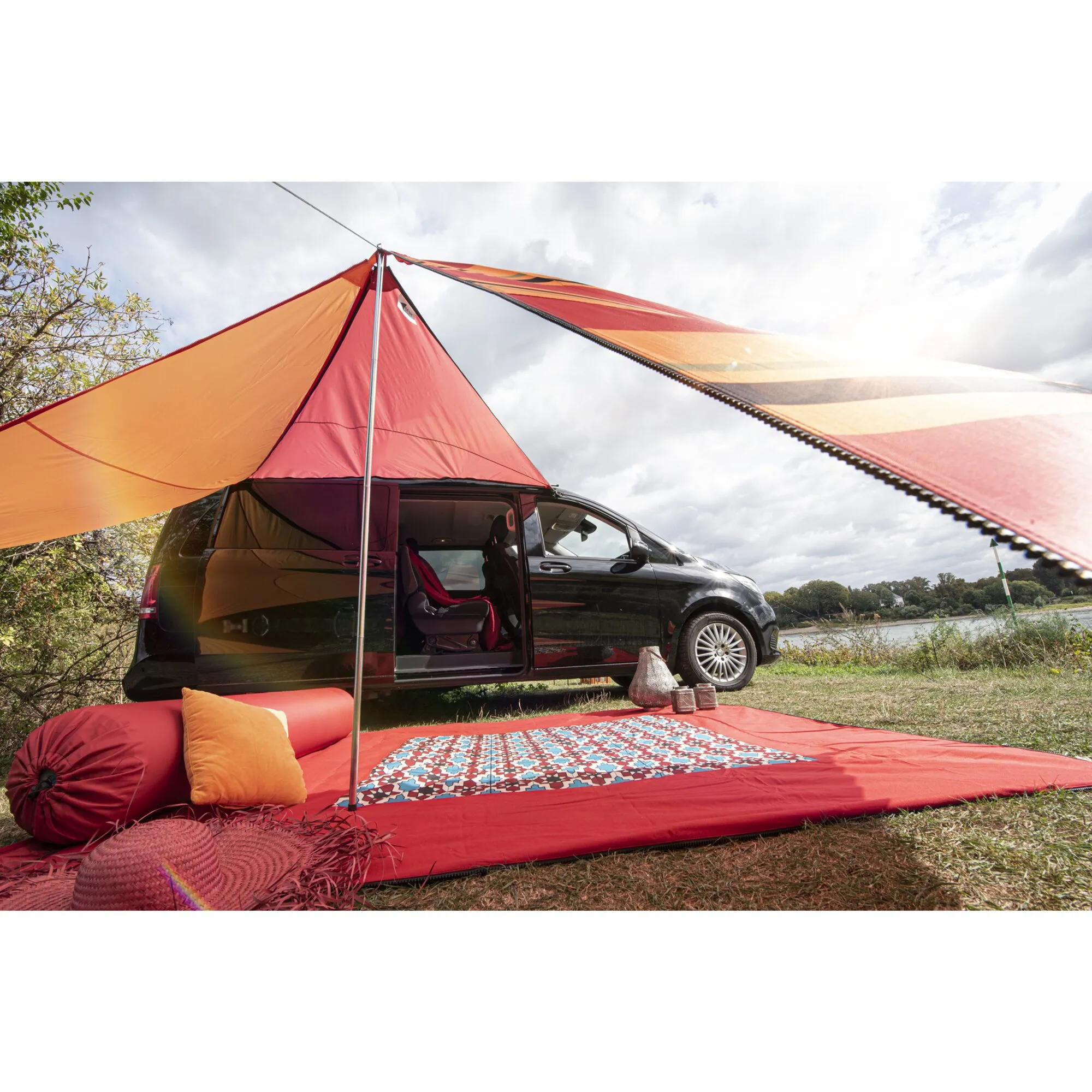 Roter Teppich Zip Carpet vor einem schwarzen Van beim Camping, mit gemustertem Mittelbereich, Sitzkissen und Sonnensegel