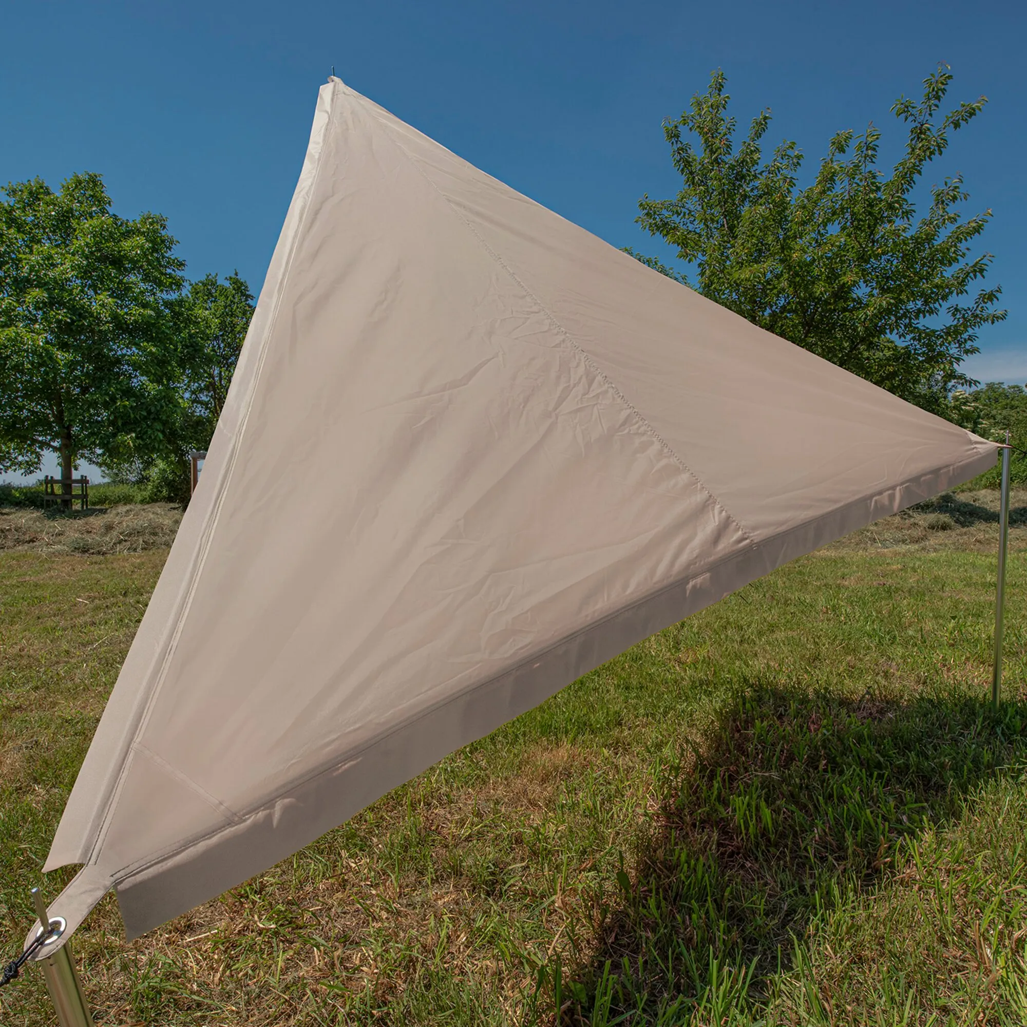 Beiges dreieckiges Sonnensegel TC Zip-Protect Canvas, zwischen Metallstangen auf einer Wiese gespannt, vor blauem Himmel und Bäumen
