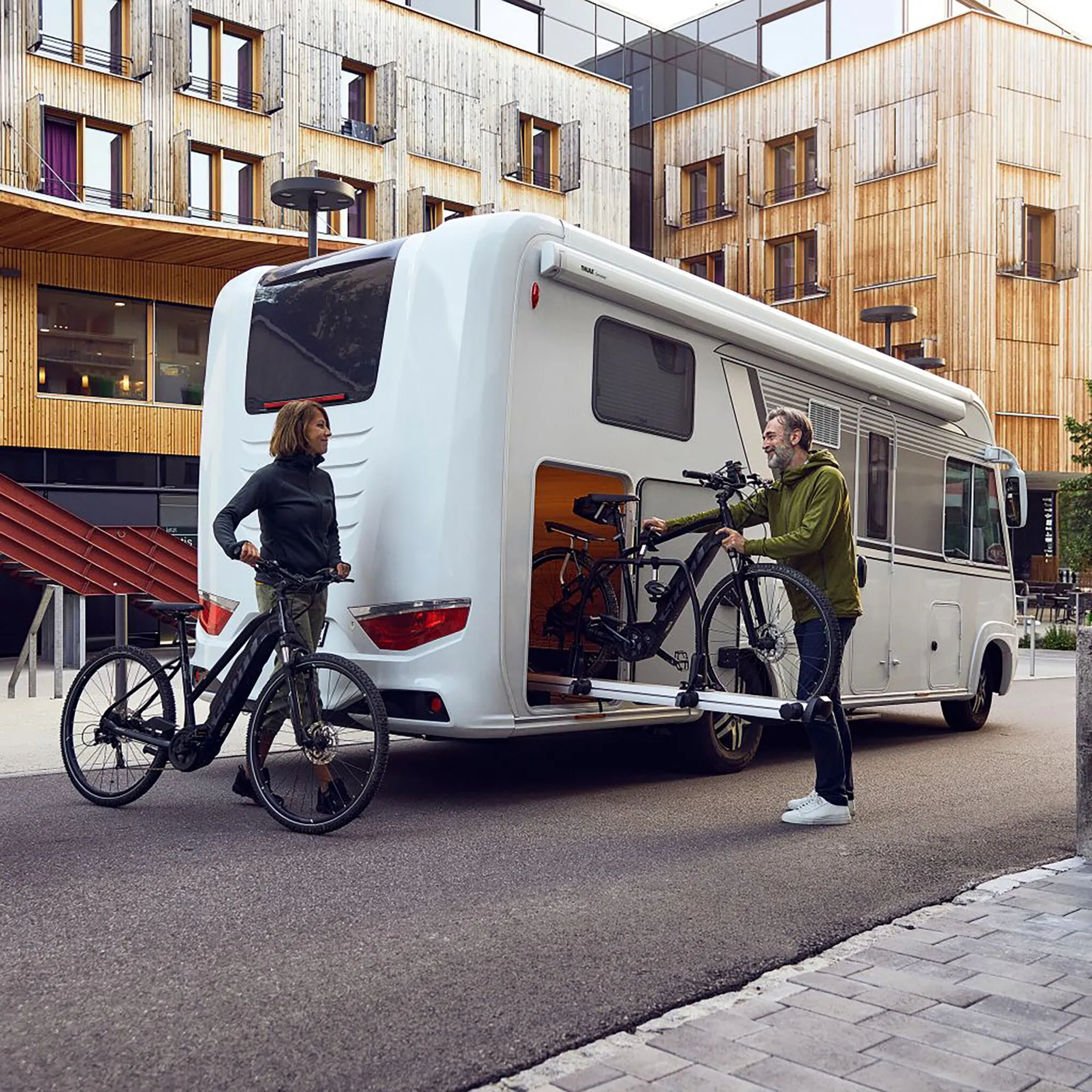 Weißes Wohnmobil mit Thule VeloSlide Fahrradträger und zwei Fahrrädern, die von einem Paar beladen werden