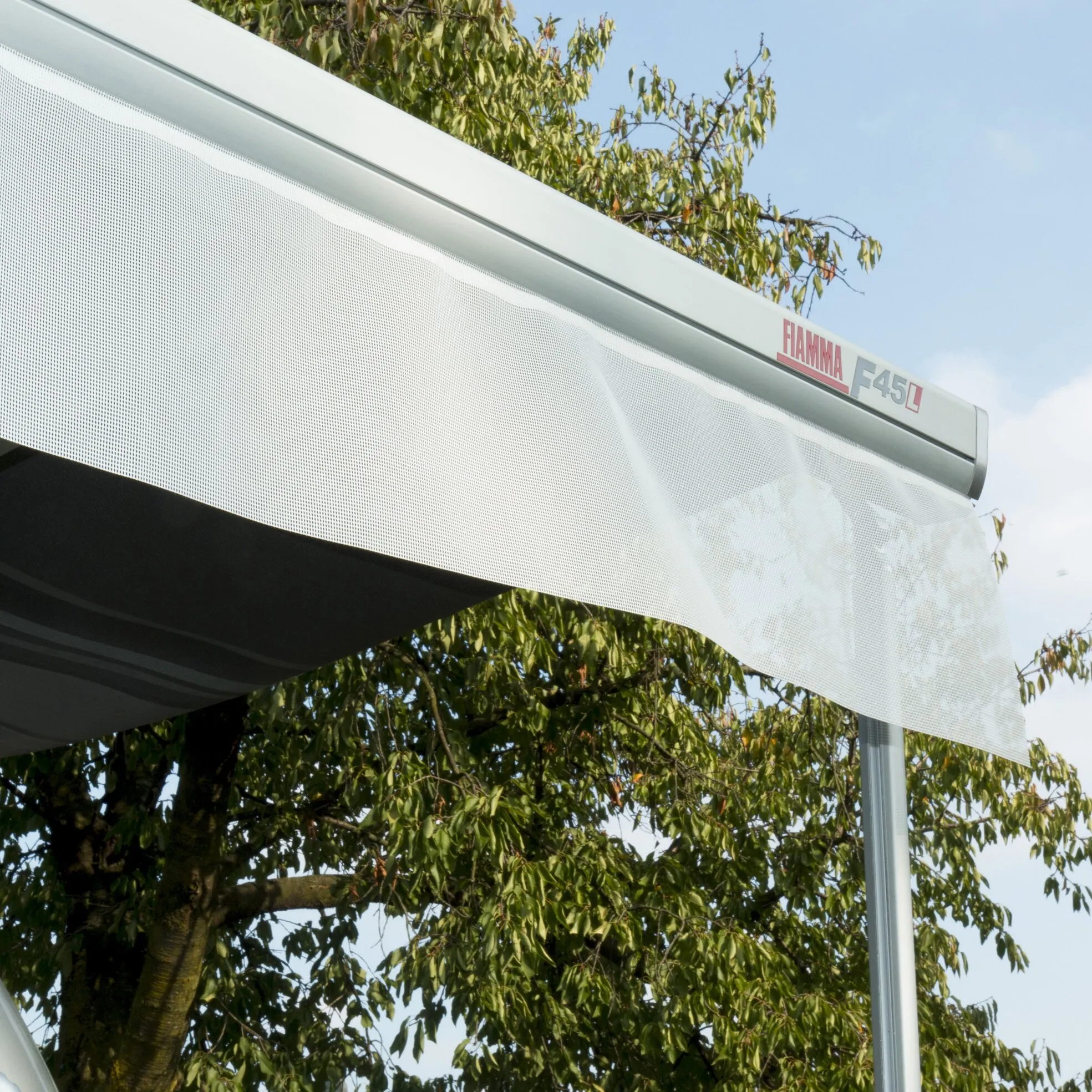 Weißer, perforierter Sonnenschutz Shade Sun View mit Fiamma F45L-Markise im Freien vor einem Baum reclined