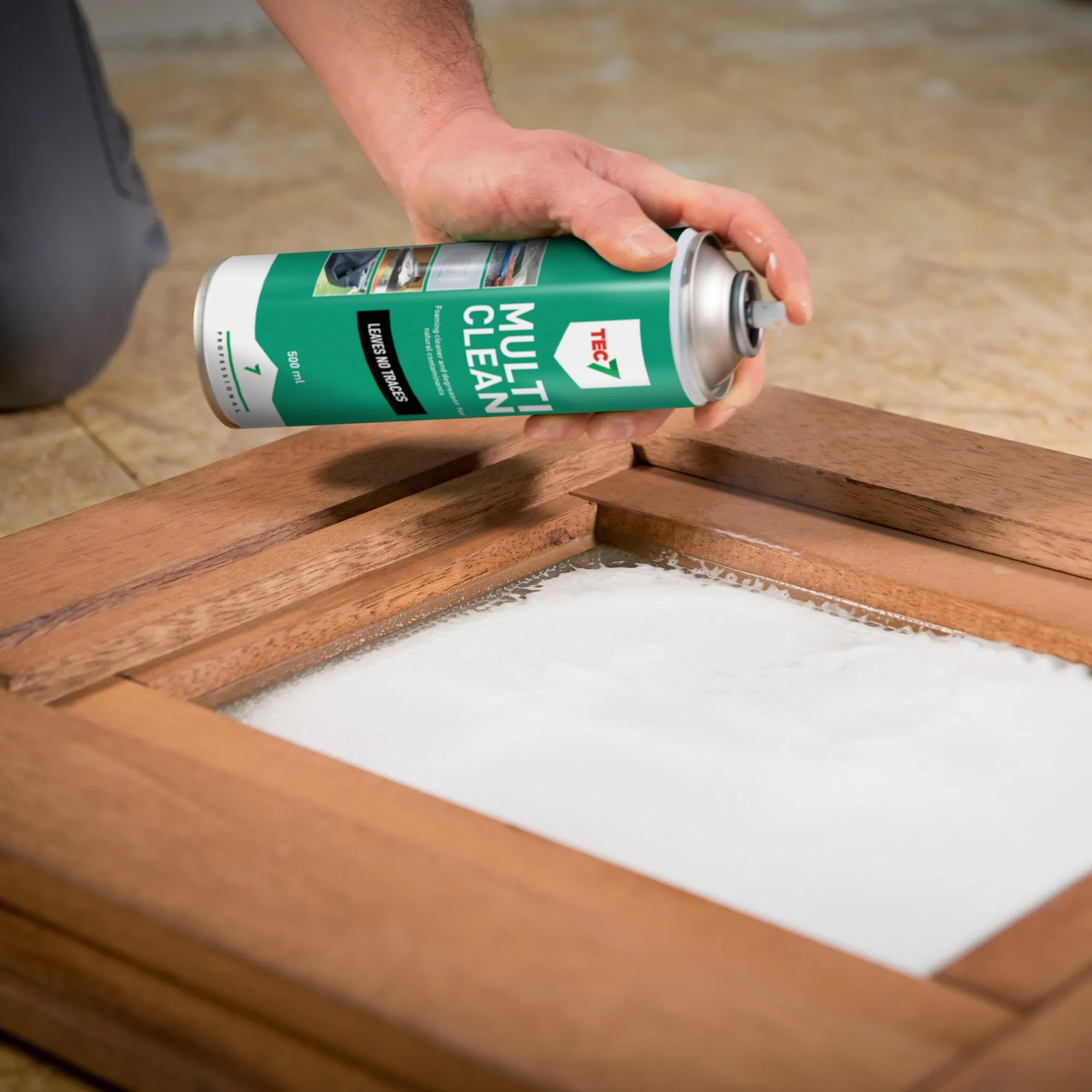 Hand hält eine grüne Sprühdose Schaumreiniger MULTICLEAN über einem mit Reinigungsschaum bedeckten Holzrahmen