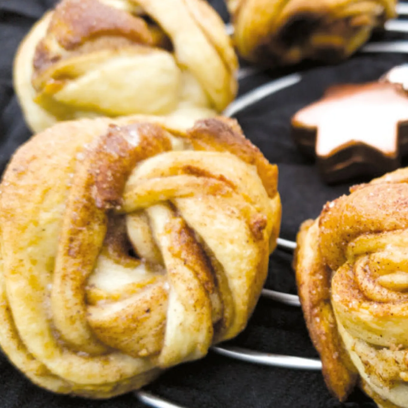 Detailaufnahme goldbrauner, spiralförmiger Plätzchen auf einem schwarzen Kuchengitter für das Backbuch Kuchen & Torten im Omnia Backofen