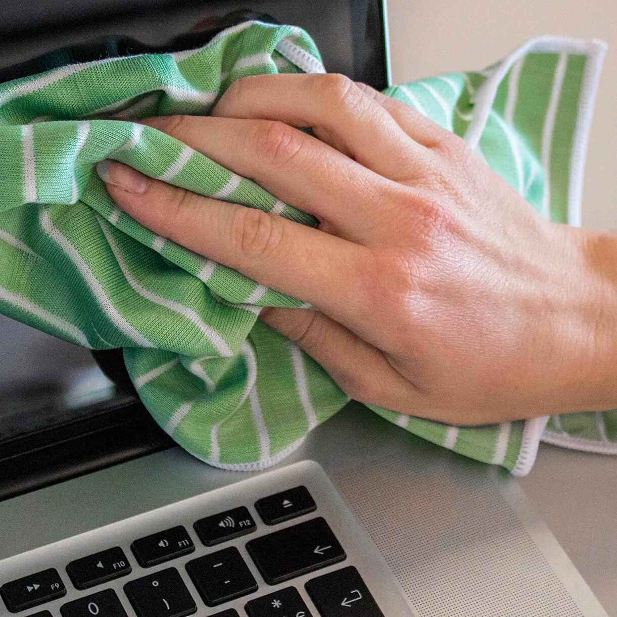 Grünes Bambustuch mit weißen Streifen wird von einer Hand zum Reinigen einer Laptop-Tastatur verwendet, weitere Tücher im Hintergrund