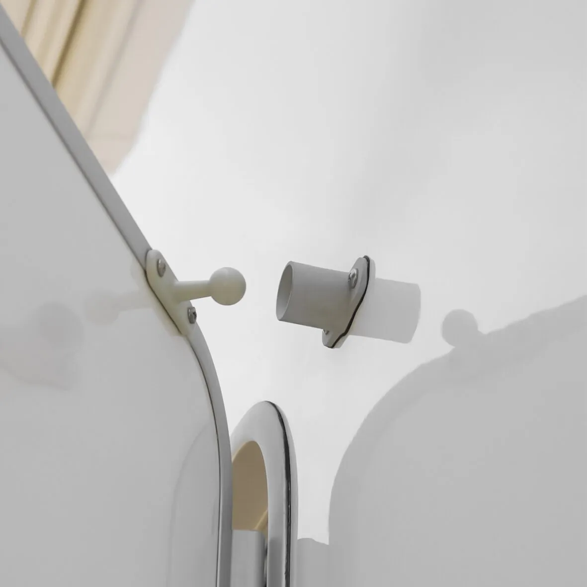 Detailaufnahme eines weißen Türfeststellers mit Kugelkopf an der Tür und zylindrischer Wandhalterung an der weißen Wand