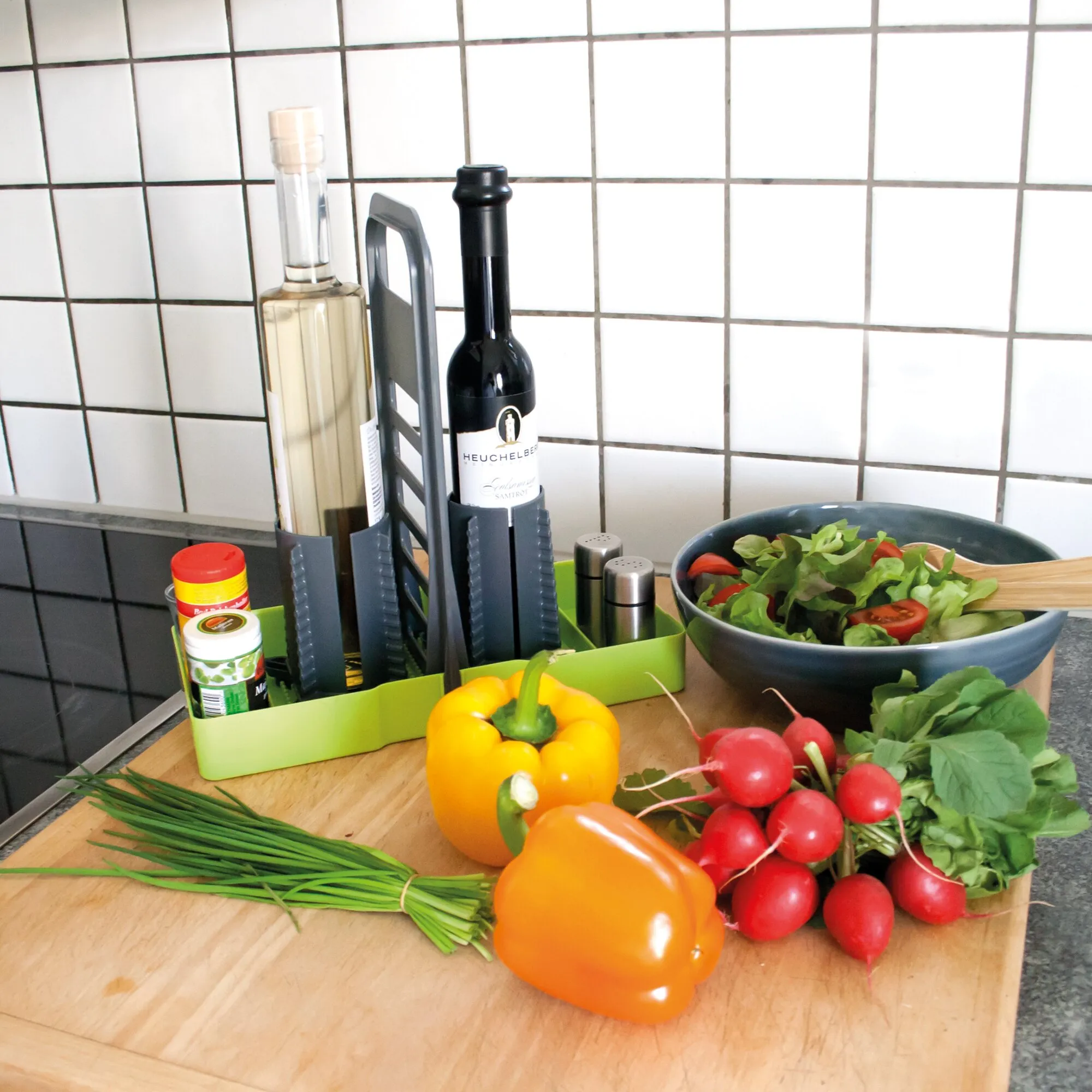 Limefarbener Multi-Tray-Flaschenhalter mit zwei Weinflaschen, Gewürzdosen und Salzstreuern auf einer Küchenarbeitsplatte voller Gemüse