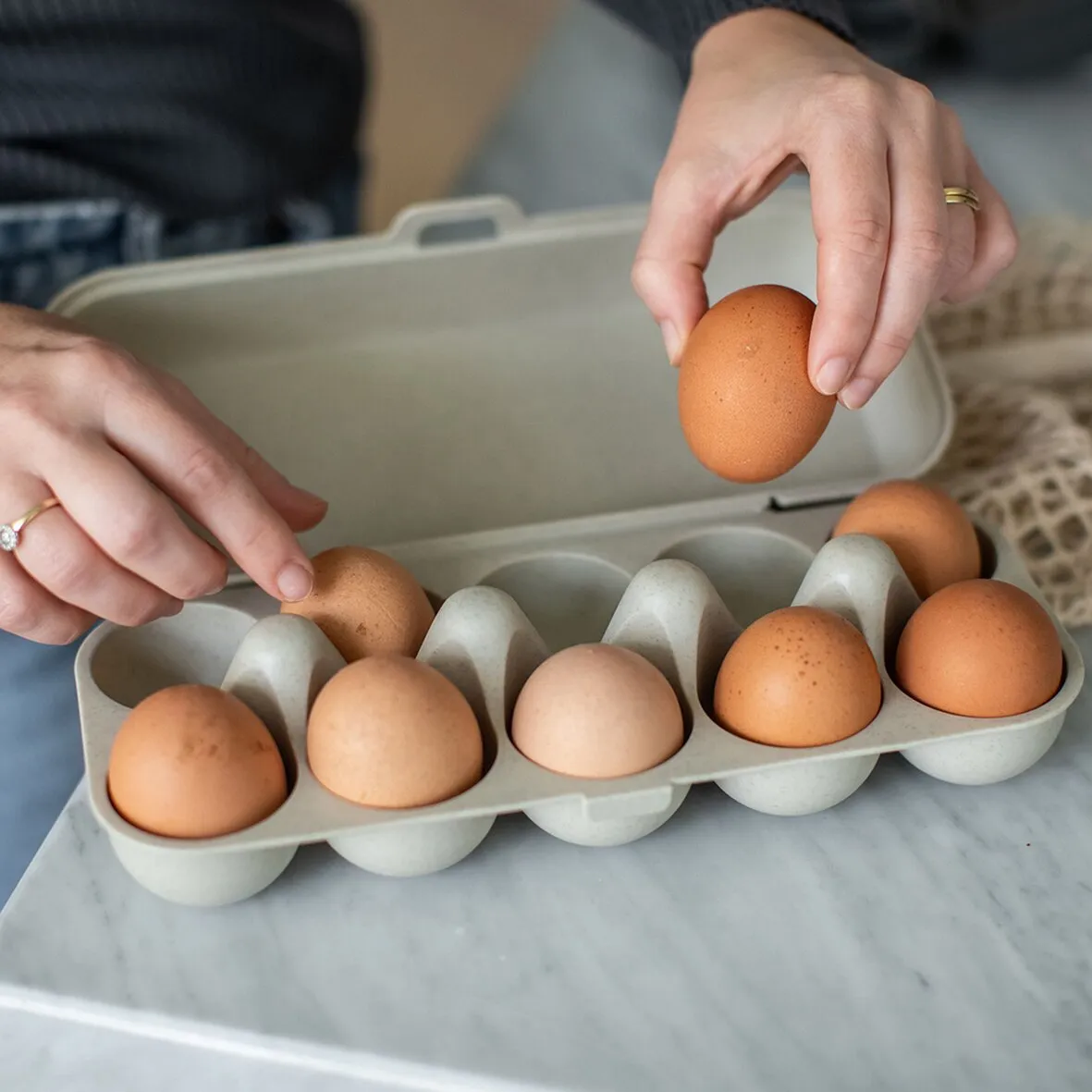 Sandfarbene Eierbox EGGS TO GO mit mehreren braunen und weißen Eiern, während ein Ei eingelegt wird