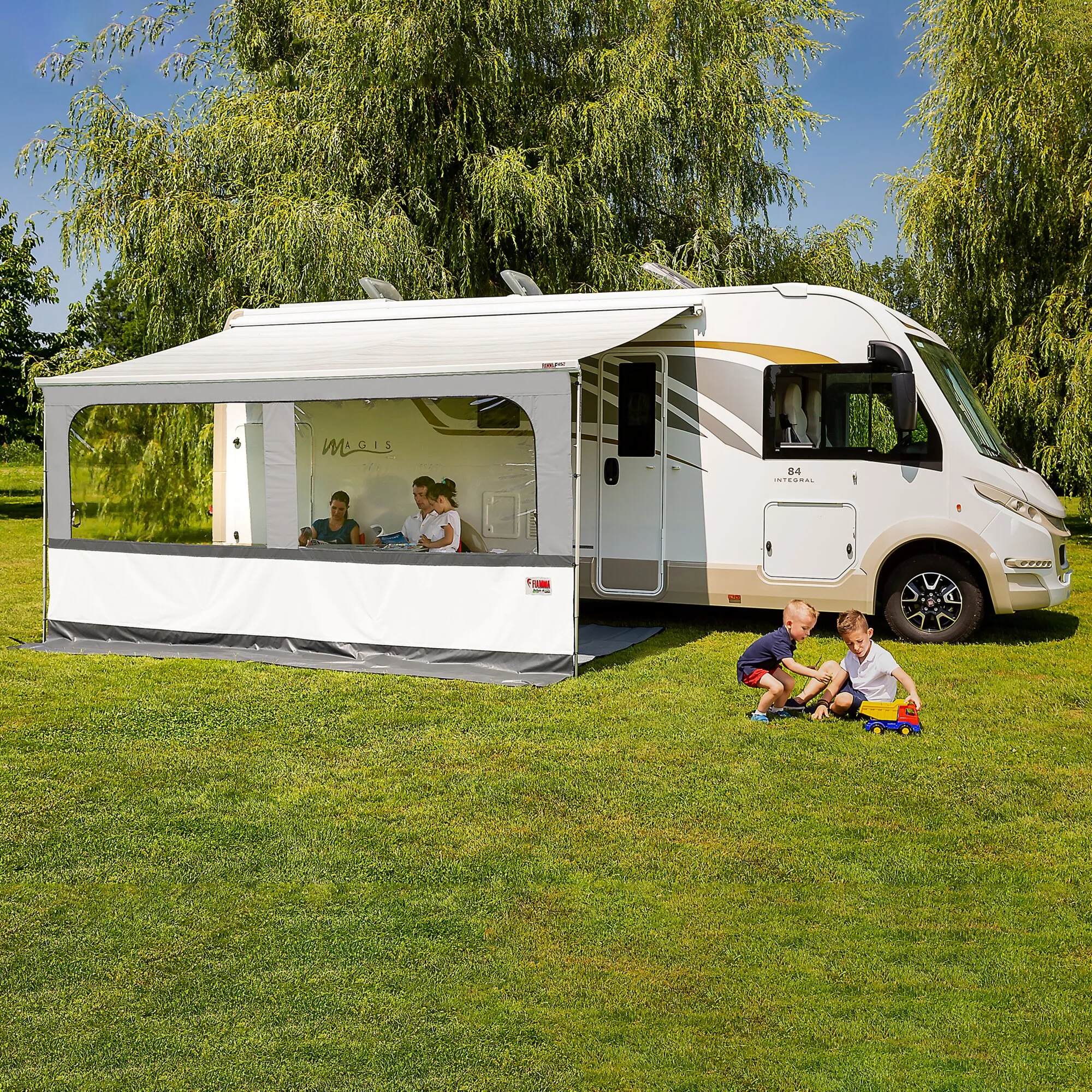 Vorderwand Blocker Pro 375 in Weiß an der Markise eines Wohnmobils, mit transparenten Fenstern auf einer Wiese mit Kindern