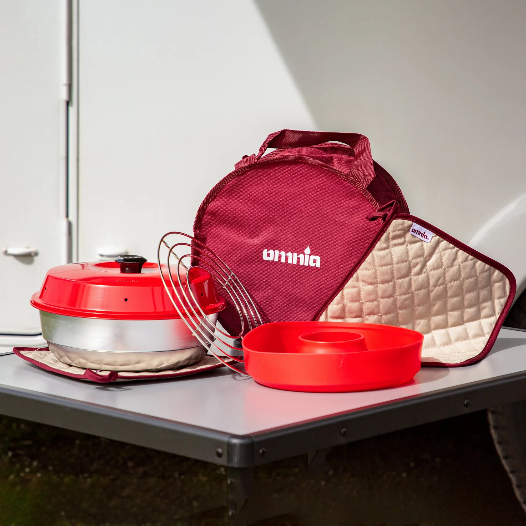 Rotes Backofen-Kit mit rundem Ofen, Backform, Gitterrost und zwei gesteppten Ofenhandschuhen auf einer Arbeitsfläche